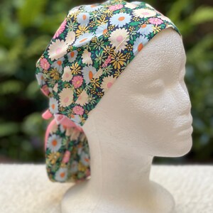 May include: A floral print surgical scrub hat with a pink tie. The hat has a dark blue background with white, pink, and yellow flowers.