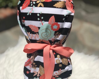 May include: A black and white striped scrub hat with a floral print in shades of pink, peach, and green. The hat has a coral ribbon tied around it.