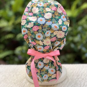 May include: A surgical cap with a floral print featuring pink, yellow, and white flowers on a dark blue background. The cap has a pink ribbon tie.