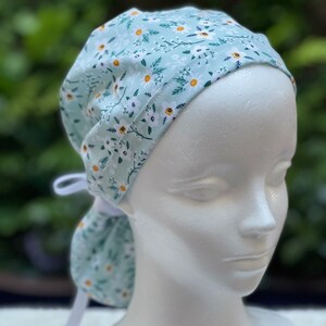 K&ouml;nnte beinhalten: Eine hellblaue OP-M&uuml;tze mit wei&szlig;em Blumenmuster. Die M&uuml;tze hat ein wei&szlig;es Band, das am Hinterkopf gebunden werden kann.