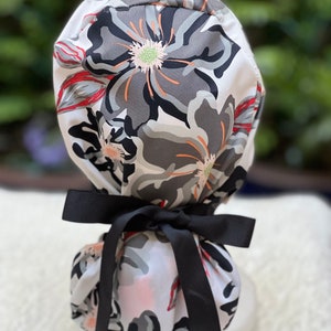 May include: A white scrub cap with a floral print in shades of gray, black, and red. The cap has a black ribbon tied around it.
