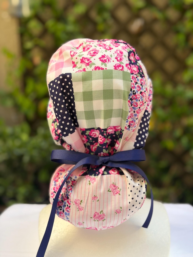 May include: A patchwork scrub cap featuring a variety of floral, polka dot, and gingham patterns in pink, navy, and green. The cap is tied with a navy blue ribbon.