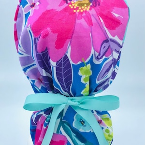 May include: A blue and pink floral print surgical scrub hat with a light blue ribbon tied around it.