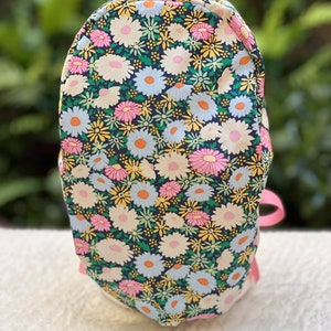 May include: A black fabric bag with a floral pattern of pink, white, and yellow daisies on a dark green background. The bag has a pink ribbon handle.