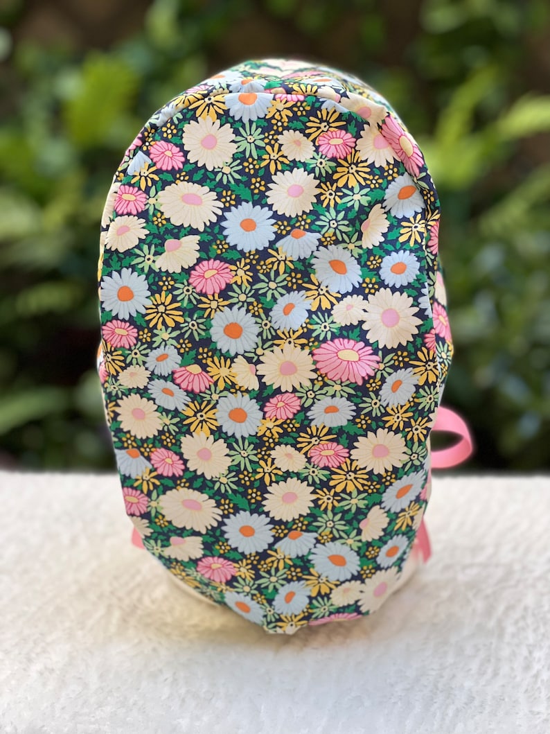 May include: A black fabric bag with a floral pattern of pink, white, and yellow daisies on a dark green background. The bag has a pink ribbon handle.