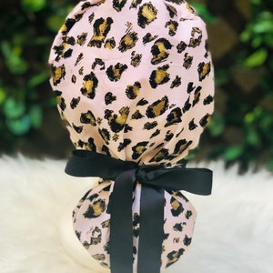 May include: Pink leopard print surgical scrub hat with black satin ties. The hat is made of a soft, comfortable fabric and is perfect for nurses, doctors, and other healthcare professionals.