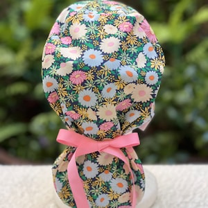 May include: A floral print surgical scrub hat with a pink ribbon tied around the bottom. The hat is made of a soft, comfortable fabric and features a variety of colorful flowers.