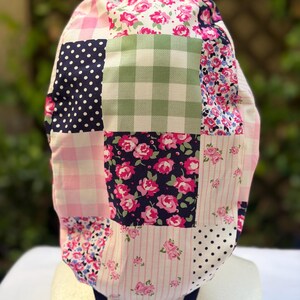 May include: A patchwork scrub cap featuring various patterns, including pink gingham, navy polka dots, and floral prints. The cap has a blue strap and is designed for medical professionals or those in similar fields.