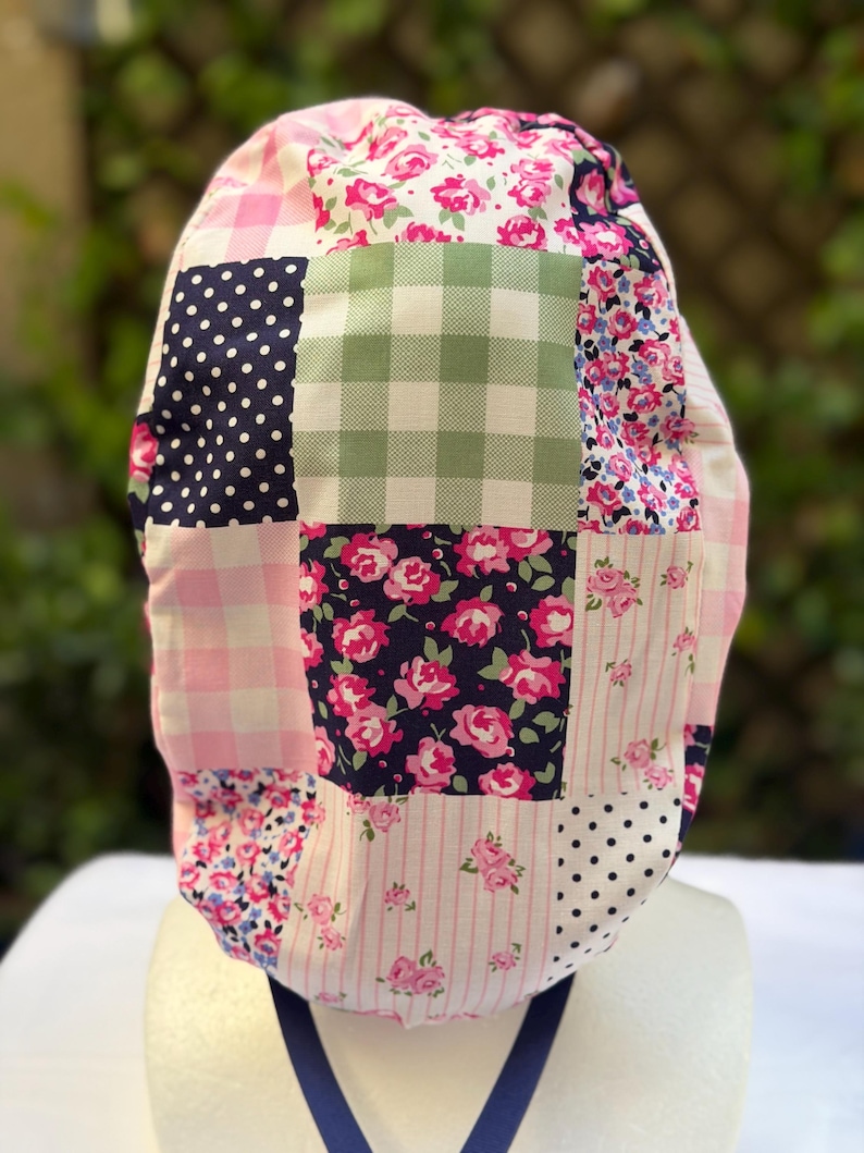 May include: A patchwork scrub cap featuring various patterns, including pink gingham, navy polka dots, and floral prints. The cap has a blue strap and is designed for medical professionals or those in similar fields.
