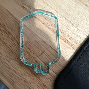 May include: A clear plastic IV bag charm with turquoise glitter embedded in the plastic.
