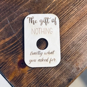 Może przedstawiać: Drewniany znak z tekstem "The gift of NOTHING Exactly what you asked for." Znak ma okrągły otwór w środku.