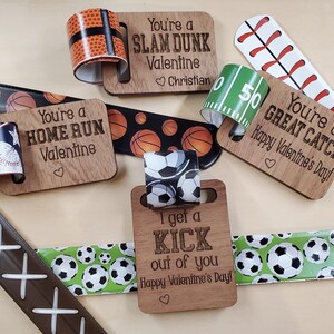 May include: Five wooden Valentine's Day cards with sports-themed designs. Each card has a different message, such as "You're a Home Run Valentine" and "I get a Kick out of you". The cards are decorated with colorful ribbons featuring basketballs, baseballs, and soccer balls.