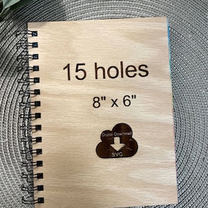 May include: A wooden notebook cover with a light wood grain finish. The cover has 15 holes for a binding system. The cover is 8 inches by 6 inches and has the text "15 holes" and "8" x 6" engraved on it. The cover also has a cloud icon with an arrow pointing down and the text "Digital Download" and "SVG" engraved on it.