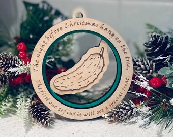 May include: A wooden Christmas ornament with a green circle in the center. The circle has a pickle inside and the text "The night before Christmas hang on the tree, The first one to find it will get a special treat." is written around the circle.