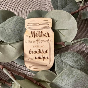 May include: A wooden cutout of a mason jar with the text "A Mother is like a flower each one beautiful and unique" engraved on it.