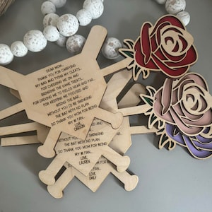 Op de afbeelding: Drie houten honkbalknuppel-versieringen met een rozenontwerp. De knuppels hebben een gegraveerde boodschap die luidt: "Lieve mama, bedankt dat je mijn tas draagt en mijn schoenen vastmaakt..."