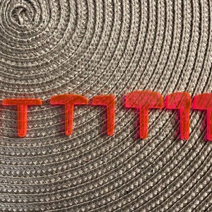 May include: Seven bright pink plastic T-shaped pieces arranged in a row on a woven surface.