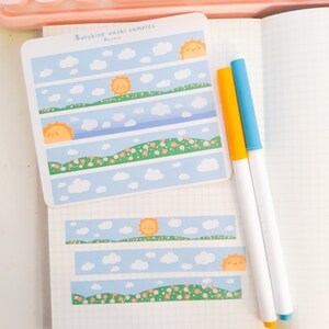 May include: Sunshine washi samples by Arriba. The washi tape features a repeating pattern of a blue sky with white clouds, a green grassy hill, and a yellow sun with a smiling face.