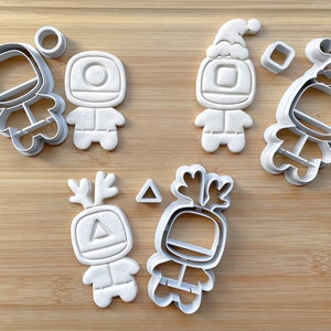 May include: A set of six white plastic cookie cutters shaped like a robot with different holiday-themed accessories. The accessories include a Santa hat, reindeer antlers, and a triangle.