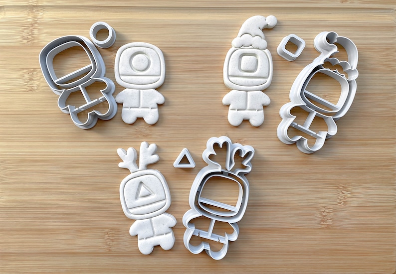May include: A set of six white plastic cookie cutters shaped like a robot with different holiday-themed accessories. The accessories include a Santa hat, reindeer antlers, and a triangle.
