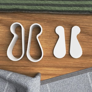 Pode incluir: Quatro cortadores de biscoitos de plástico branco em forma de borboleta e duas formas de lágrima. Os cortadores estão sobre uma superfície de madeira.