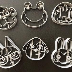 Puede incluir: Conjunto de seis cortadores de galletas de pl&aacute;stico blanco con forma de personajes de animales. Los personajes incluyen una rana, un mono, un conejo, un gato, un perro y una ardilla.