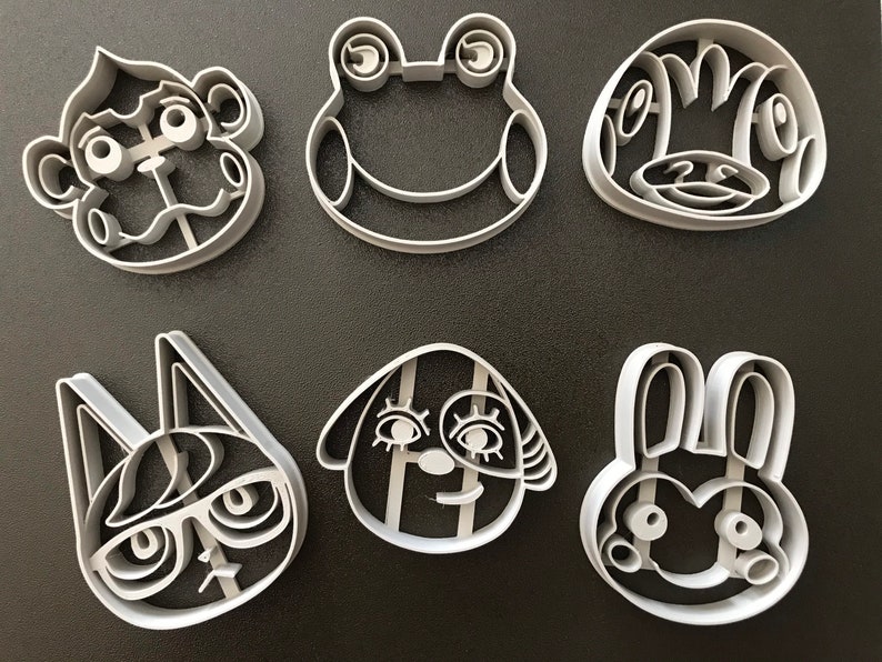 Puede incluir: Conjunto de seis cortadores de galletas de pl&aacute;stico blanco con forma de personajes de animales. Los personajes incluyen una rana, un mono, un conejo, un gato, un perro y una ardilla.