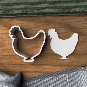 May include: Two white plastic cookie cutters shaped like chickens on a wooden surface.