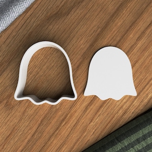 Puede incluir: Dos cortadores de galletas de plástico blanco con forma de fantasmas. El fantasma de la izquierda tiene un borde inferior ondulado y el fantasma de la derecha tiene un borde inferior recto.