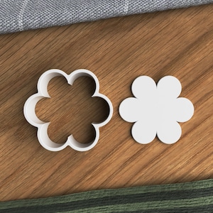 Könnte beinhalten: Zwei weiße Plastik-Ausstecher in Form einer Blume mit fünf Blütenblättern. Die Ausstecher liegen auf einer Holzoberfläche.