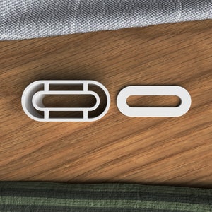 May include: Two white plastic curtain rings. One ring is oval shaped with a smaller oval cut out in the center. The other ring is a simple oval shape.