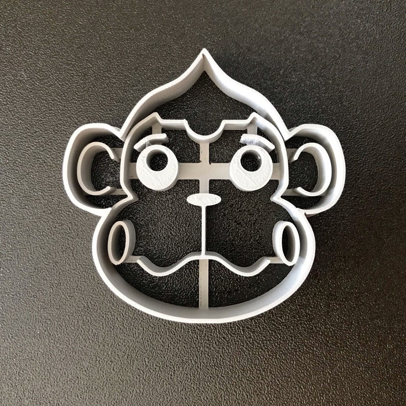 Puede incluir: Un cortador de galletas de pl&aacute;stico gris en forma de cara de mono. El mono tiene ojos grandes, una nariz peque&ntilde;a y una boca ancha.