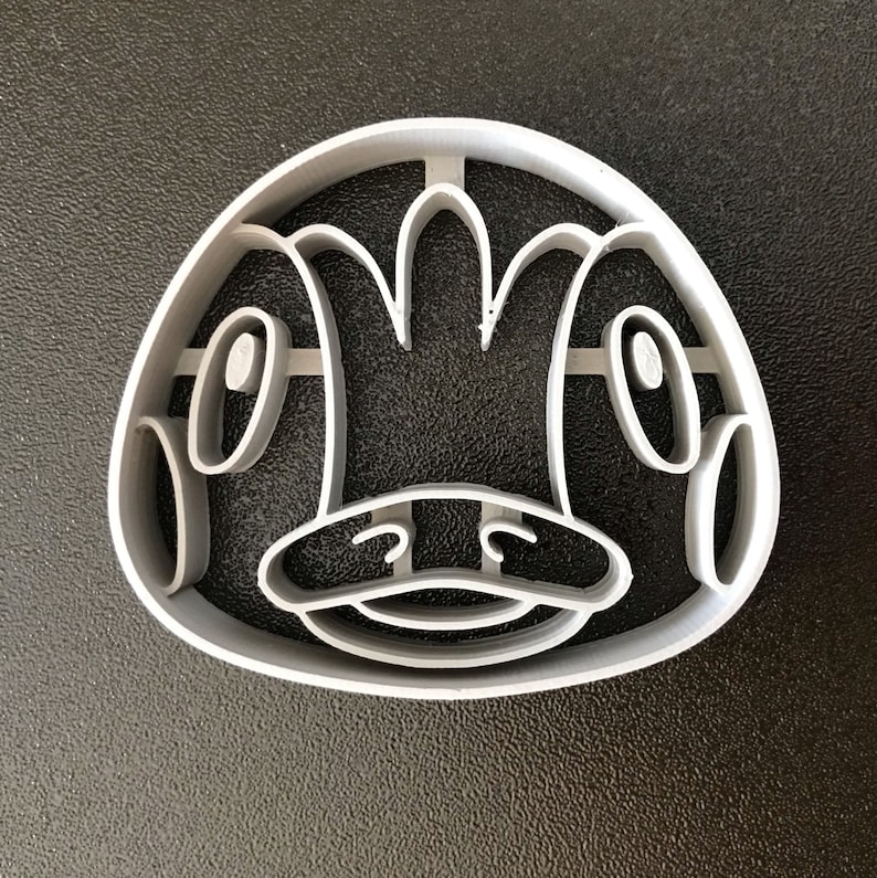 Puede incluir: Un cortador de galletas de pl&aacute;stico gris con forma de animal de dibujos animados con un pico grande y ojos. El animal tiene una forma de corona en la cabeza.