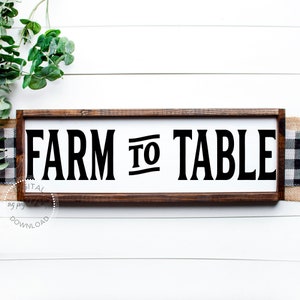 May include: A wooden sign with a white background and black text that reads "FARM TO TABLE". The sign is framed in a dark brown wood frame.