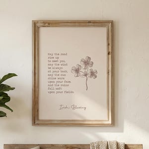 May include: A cozy living room scene with a wooden bench, pillows, and a woven throw. A framed print with text and a floral illustration hangs on the wall. A large potted plant and a side table with a lamp add to the warm ambiance.