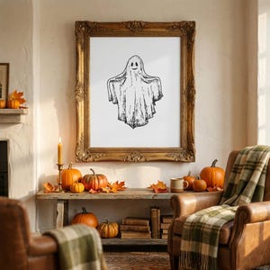 Vintage pencil sketch of smiling ghost on white background displayed in large ornate gold baroque wooden frame in cozy cottagecore fall living room with rustic wooden bench covered in orange pumpkins, autumn leaves, lit beeswax candle in brass holder, old books, ceramic mug and green plaid throw on leather armchairs — cottagecore ghost halloween wall art digital download, perfect for cute halloween decor, fall home decor, spooky cottagecore or halloween living room art