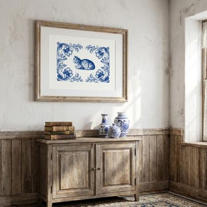 May include: A framed print with a blue and white cat illustration and floral border. The artwork is above a wooden cabinet with vases and books. The room has a vintage style, with wooden paneling and a patterned rug.