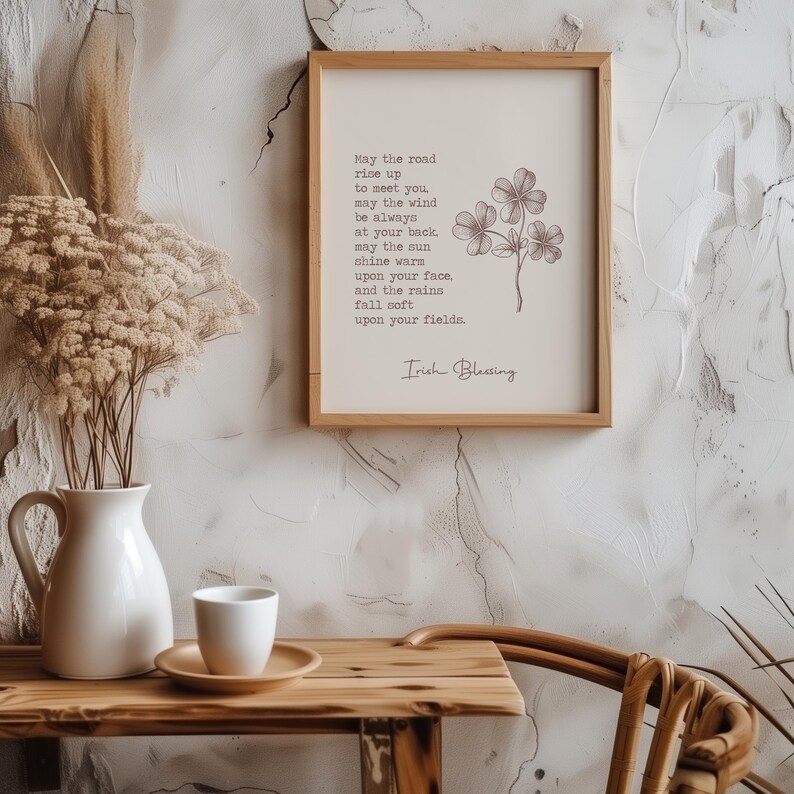 May include: A framed print with an Irish blessing, featuring a light beige background and a brown wooden frame. The text includes a poem and a shamrock illustration. A white vase, cup, and saucer are on a wooden table.