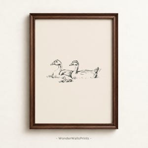 May include: A framed wall art print featuring a black ink line drawing of two adult geese and one gosling resting in grass on a cream-colored background. The artwork is enclosed in a dark brown wooden frame. The text WonderWallsPrints is visible.