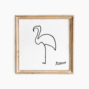 May include: A framed print with a minimalist black line drawing of a flamingo on a white background. The artwork is signed "Picasso" in the lower right corner. The frame is a light brown colour.