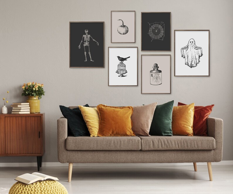 May include: A living room featuring a grey sofa with cushions in shades of green, orange and brown. The wall behind the sofa is adorned with black and white framed prints depicting a skeleton, a bird in a cage, a pumpkin, a spiderweb, a bottle of potion and a ghost.