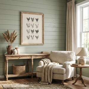 May include: A framed print featuring illustrations of various chicken breeds hangs above a wooden console table. The room has a neutral color palette with a beige armchair, a woven basket, and a decorative lamp. The wall is painted a muted green.