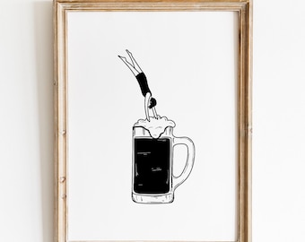 May include: A framed black and white line art print featuring a person diving headfirst into a large glass beer mug filled with dark liquid and topped with foam. The artwork is enclosed in a light-coloured wooden frame with a simple, clean design.