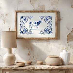 Puede incluir: Una impresión enmarcada con una ilustración de vaca azul y blanca. La vaca está centrada sobre un fondo blanco, rodeada de diseños florales azules. El marco de madera clara añade un toque rústico a la obra de arte.