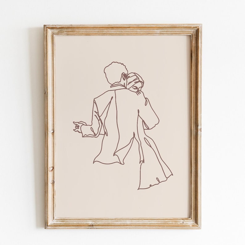 May include: A framed wall art print featuring a dark brown continuous line drawing of two figures embracing on a light beige background. The artwork is enclosed in a light-colored wooden frame with a visible grain, showcasing a couple in a dance.