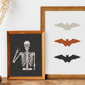 May include: Two framed prints, one with a skeleton giving a peace sign and the other with three bats in different colours: grey, orange, and black.