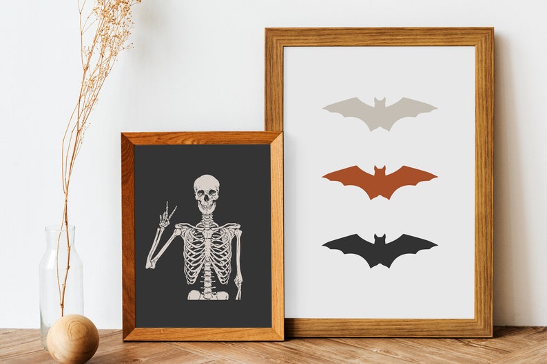 May include: Two framed prints, one with a skeleton giving a peace sign and the other with three bats in different colours: grey, orange, and black.