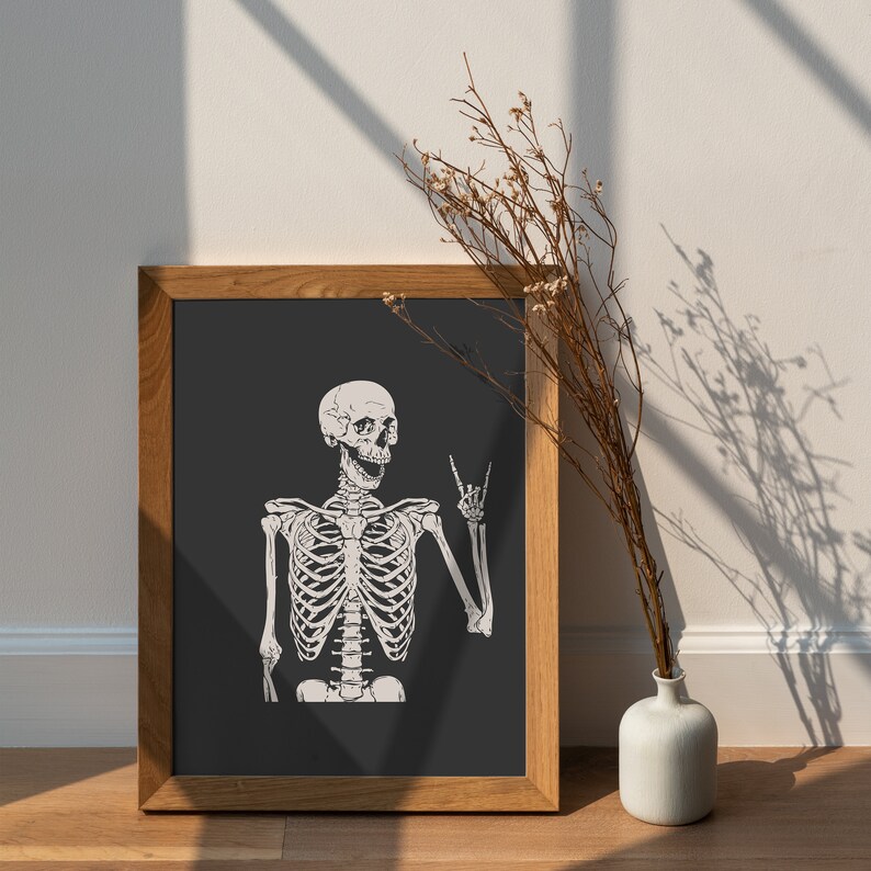 May include: A framed wall art print featuring a white skeleton illustration on a dark gray background. The skeleton is depicted with an open mouth and one hand raised in a rock and roll hand gesture. The print is encased in a light brown wooden frame.
