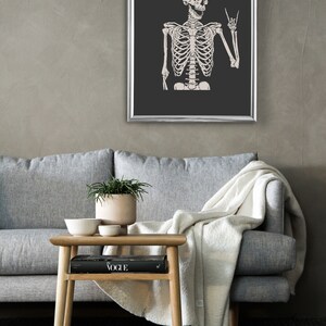 May include: A framed wall art print featuring a light-colored human skeleton illustration against a dark charcoal background. The skeleton is depicted from the waist up with its mouth open and one hand raised in a rock and roll hand gesture.