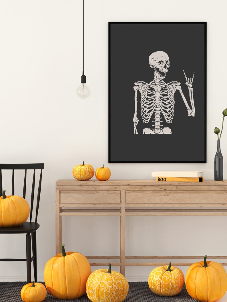 May include: A framed wall art print featuring a light-colored human skeleton illustration on a dark gray background. The skeleton is depicted from the waist up, with its left hand raised in a rock-and-roll hand gesture, set against a solid black frame.